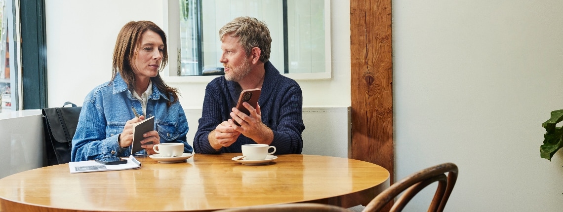 A couple sitting at a café table look at a phone and try to determine if they were affected by the latest data breach.