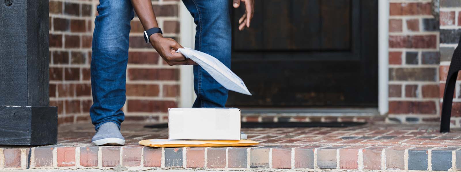 A person picks up packages off of their front porch that are part of a brushing scam.