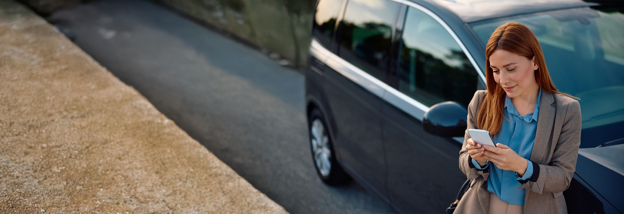 A woman on her smartphone while standing next her car.