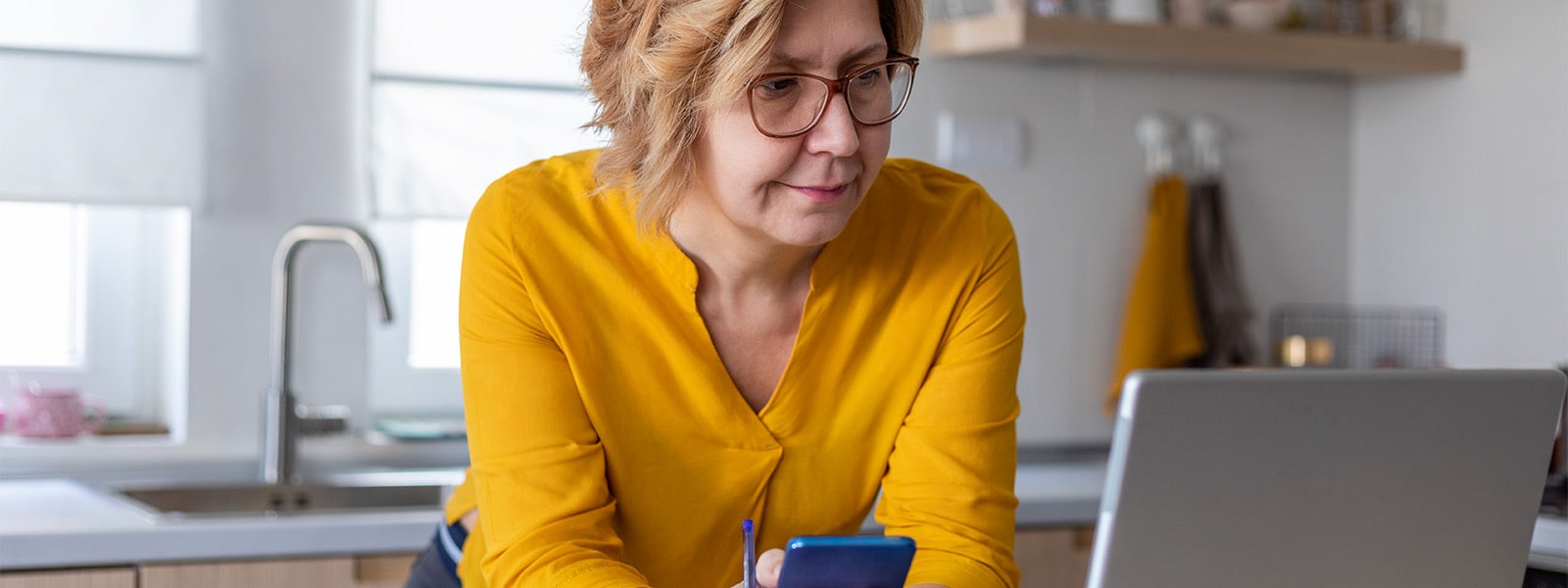 A woman looking at her laptop and phone, researching the differences between credit locks and freezes to protect her financial security.