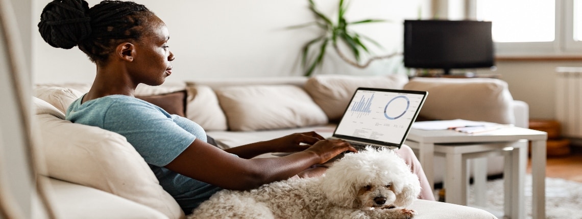 Image of a woman witting on a couch with a dog and her laptop.