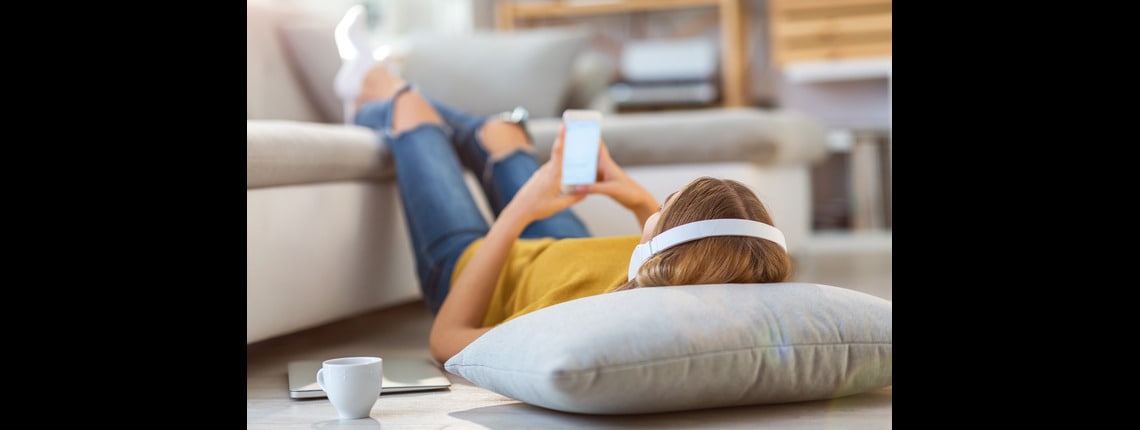 A person laying down, wearing headphones and holding a mobile device