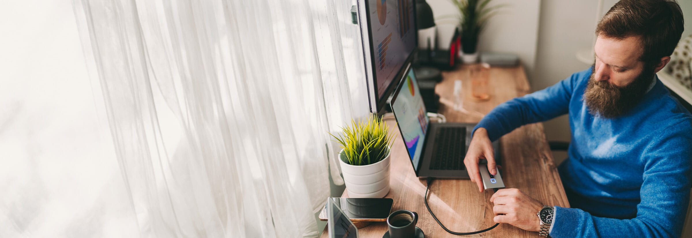 A person sitting at a desk plugging an external hard drive into a laptop.
