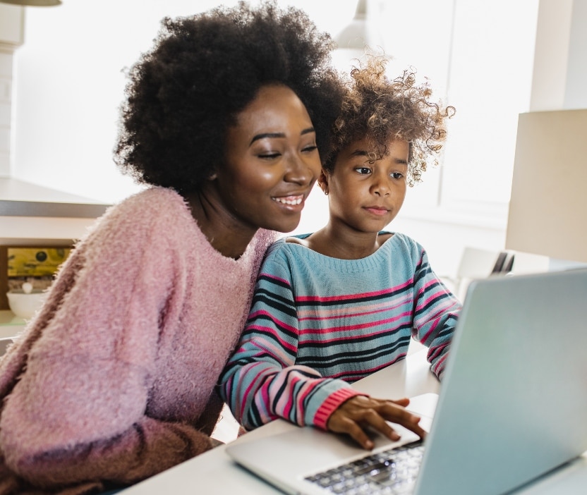 A woman and her child sit in front of a laptop computer, learning about Safer Internet Day together.