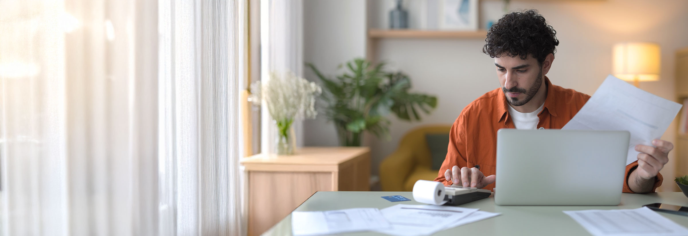A man at a table uses a laptop and papers to organize and review his tax impressions.