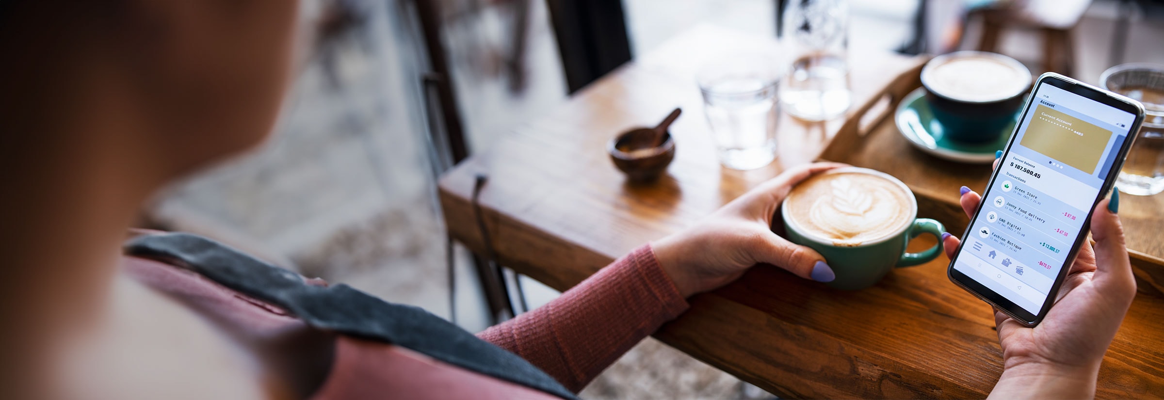 A woman in a cafe looking at a banking app on her phone.