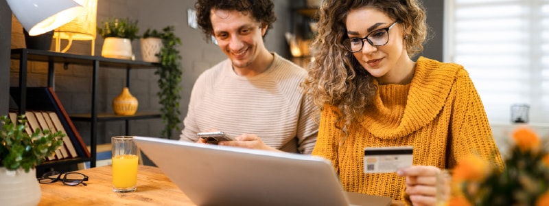 A man and woman look at a computer with a credit card in hand, likely curious about what is a CVV number.