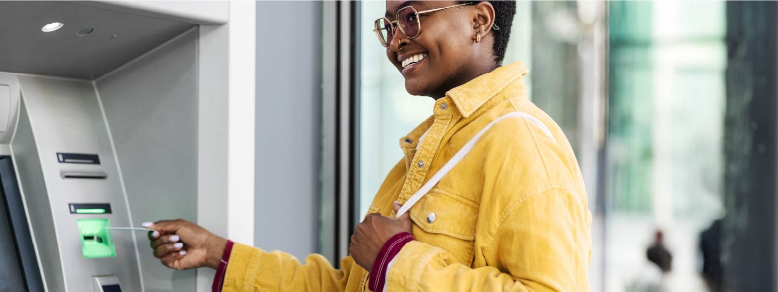 A smiling woman inserts her credit or debit card into an ATM after learning how to avoid wire transfer scams.