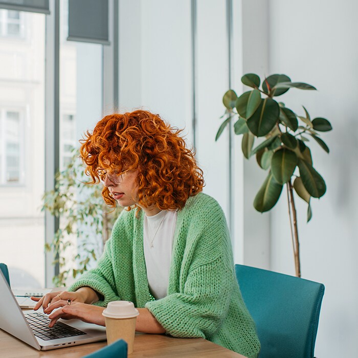 A woman sitting at a desk by the window on her laptop.