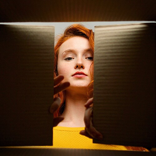 A woman peering into a box to see a fake product she’s received after being scammed on eBay.