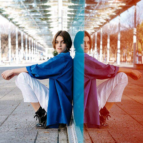 A young woman leaning against a mirror, which shows her reflection.