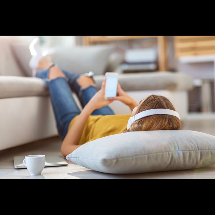 A person laying down, wearing headphones and holding a mobile device