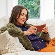 A woman sits on her couch, looking at her phone as she navigates the aftermath of identity theft.