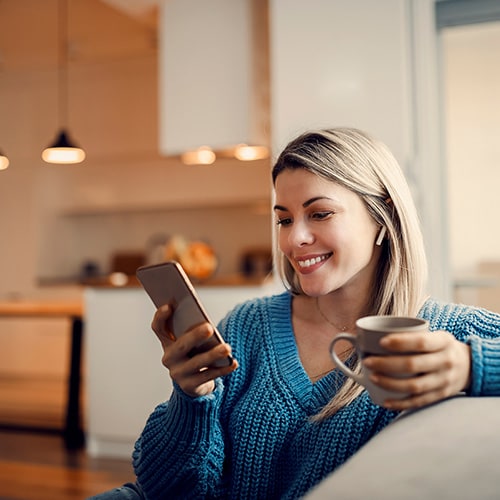 A woman sits on her couch, looking at her phone as she navigates the aftermath of identity theft.