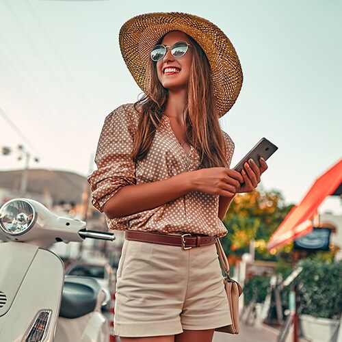 A person sitting down, wearing headphones, and holding a mobile device by a beach