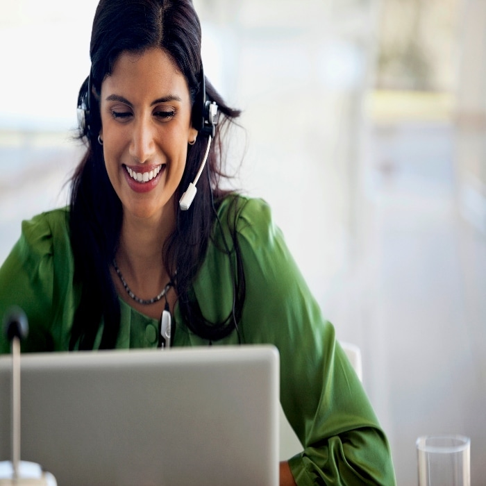 A woman in a green shirt wearing a headset and sitting at a computer.