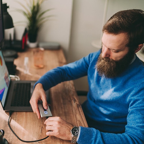 A person sitting at a desk plugging an external hard drive into a laptop.
