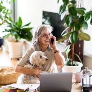 Woman taking happily on the phone with her white dog in hand.