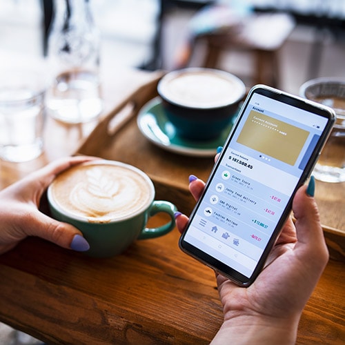 A woman in a cafe looking at a banking app on her phone.